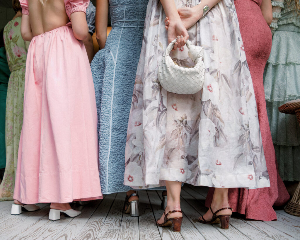 A colorful image of a group of wedding guests and their beautiful dresses. This image only features the subjects from the waist down. This photo is an example of how luxury wedding photographers hide in plain sight to achieve great photographic results.